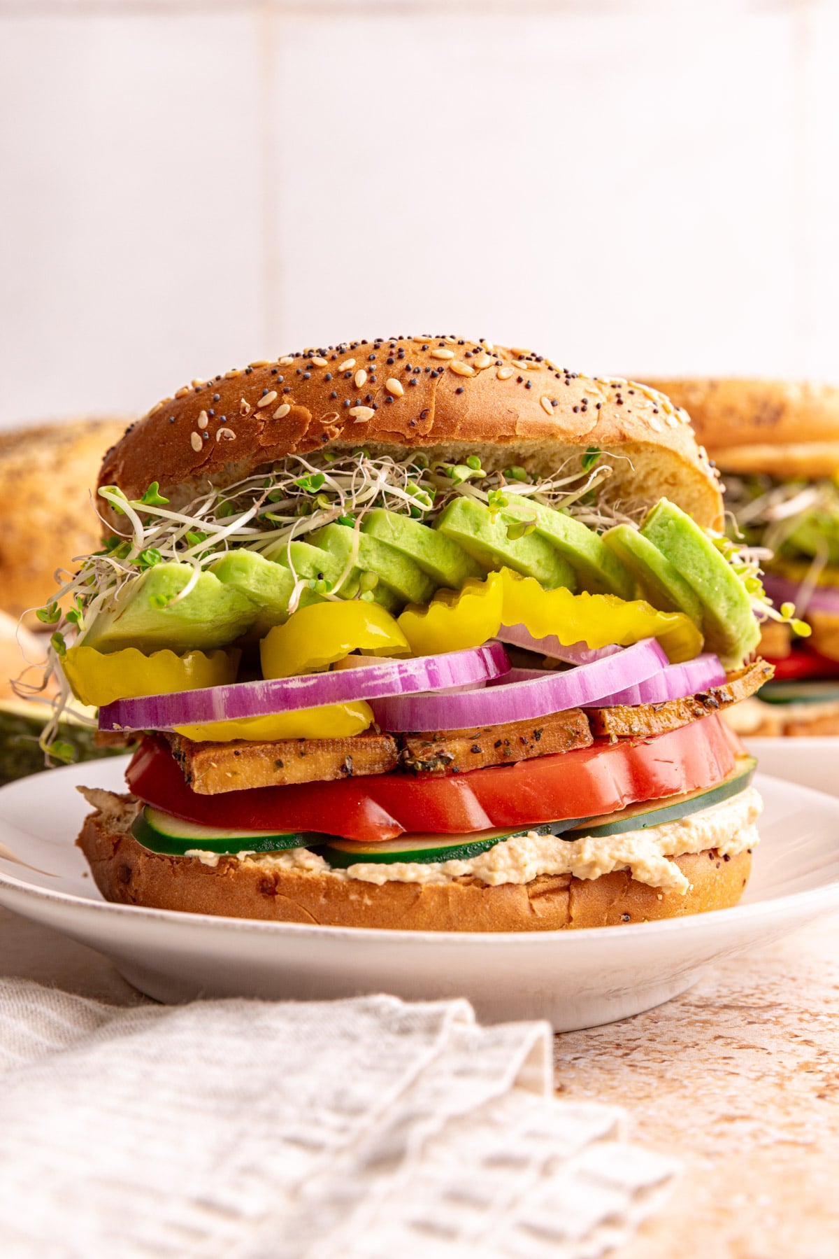 A loaded hummus bagel sandwich on a plate ready to eat.