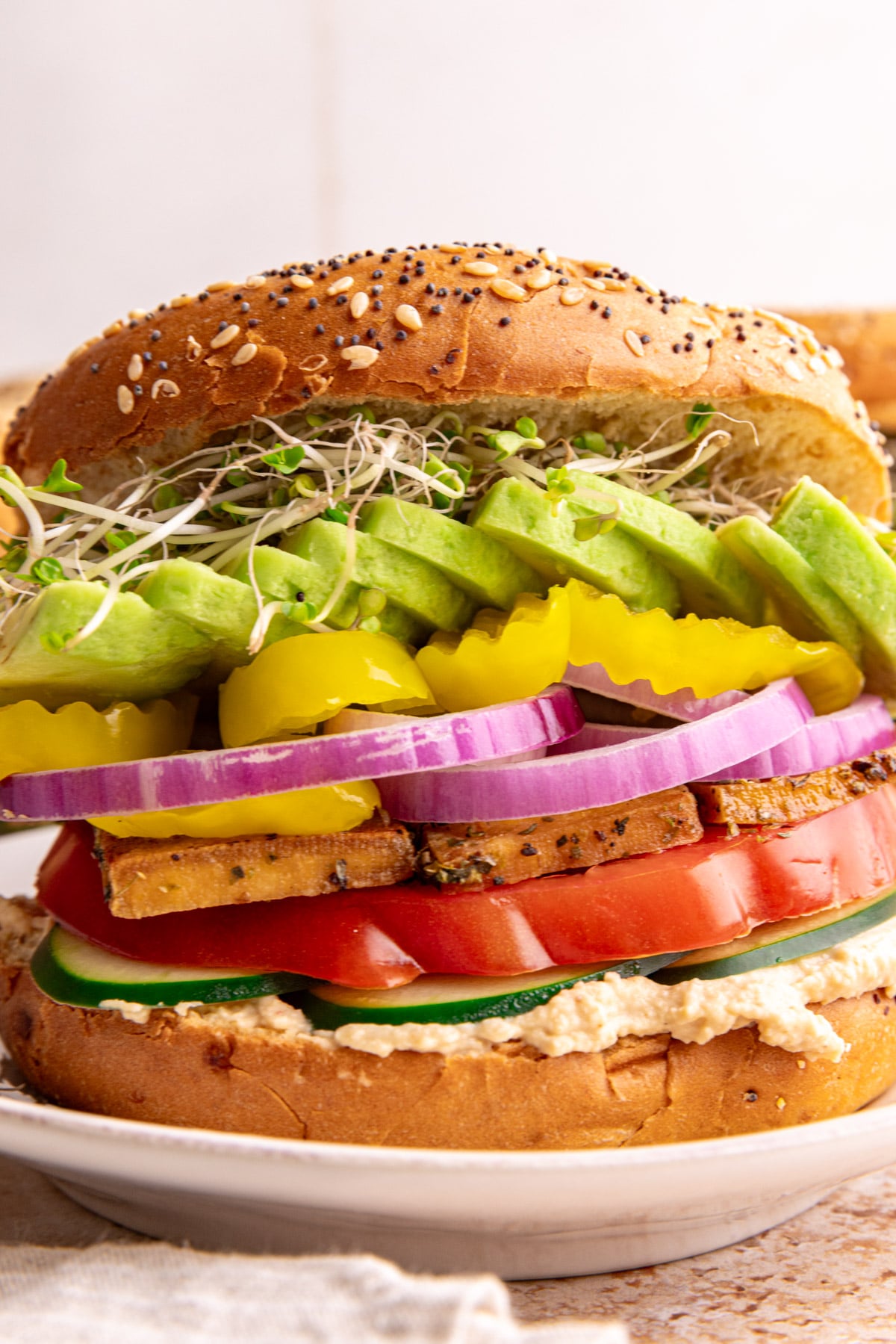 A loaded hummus bagel sandwich on a plate ready to eat.