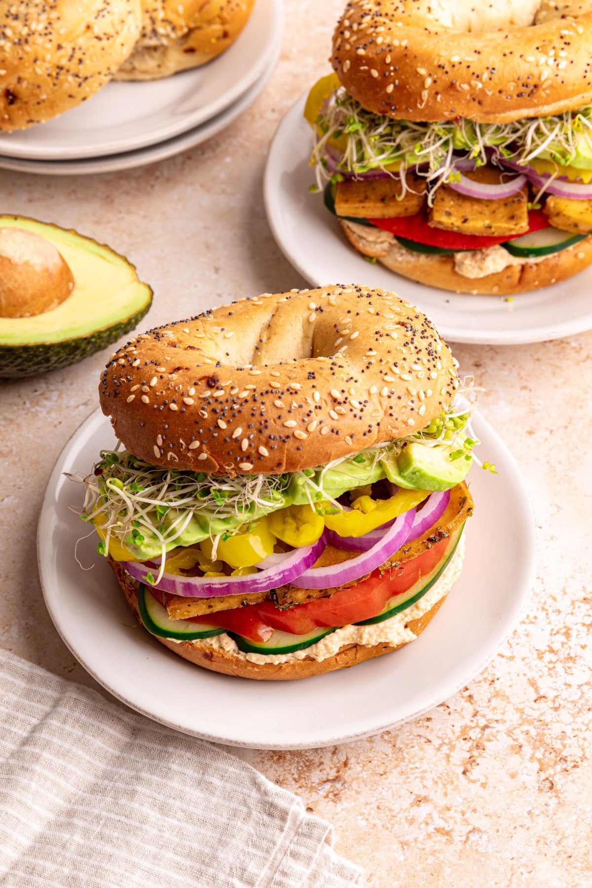 A loaded hummus bagel sandwich on a plate ready to eat.