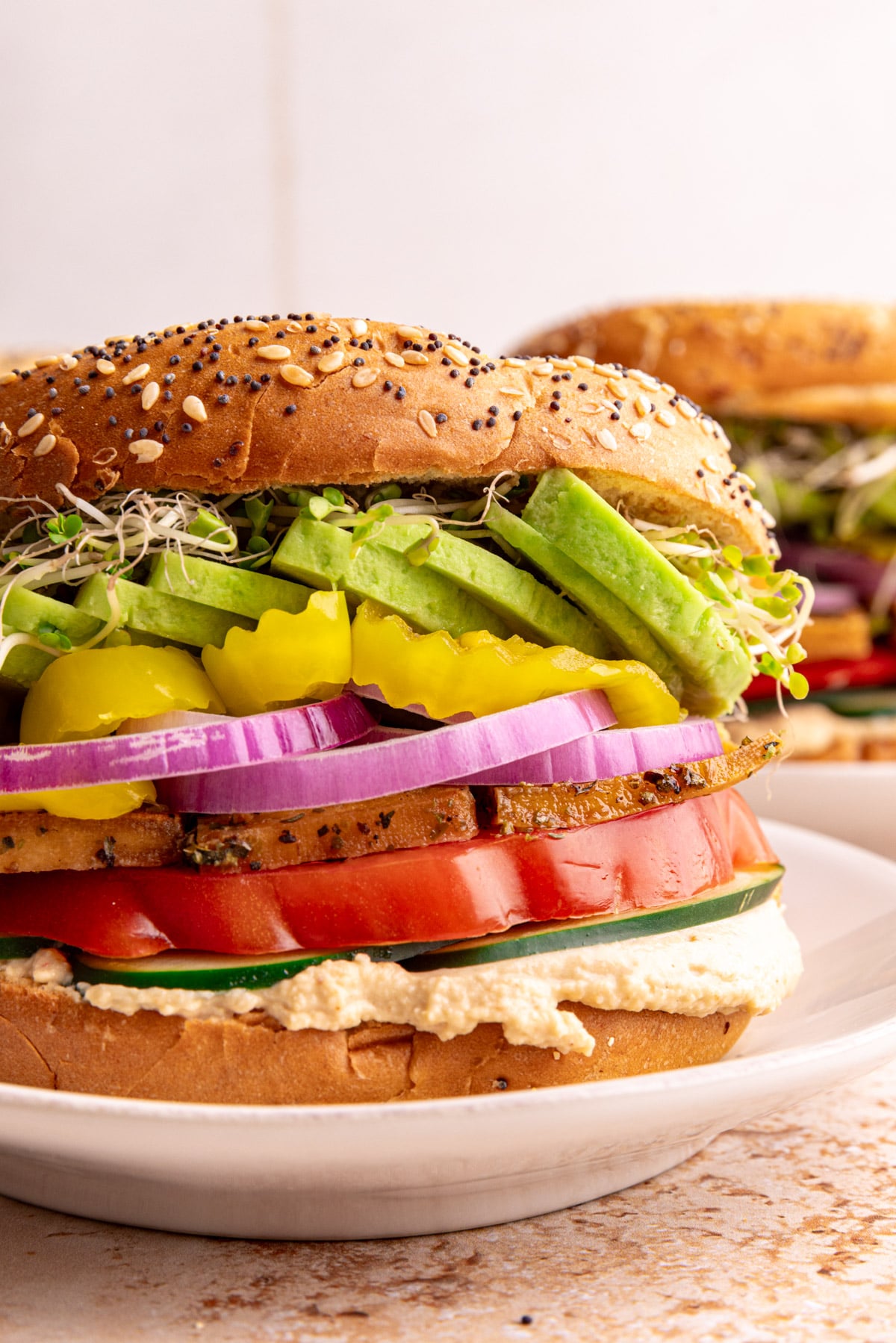 A loaded hummus bagel sandwich on a plate ready to eat.