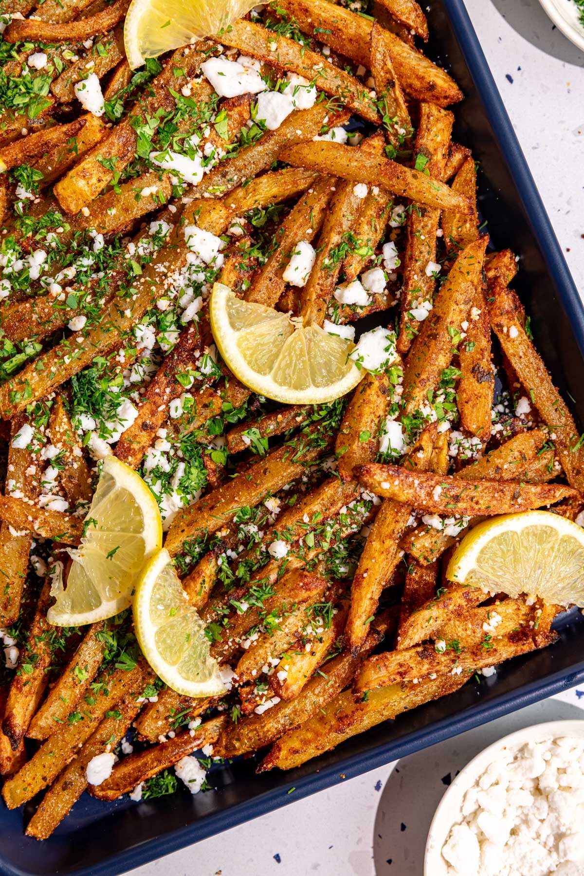 Lemons, herbs, and feta on a tray of loaded greek feta fries.