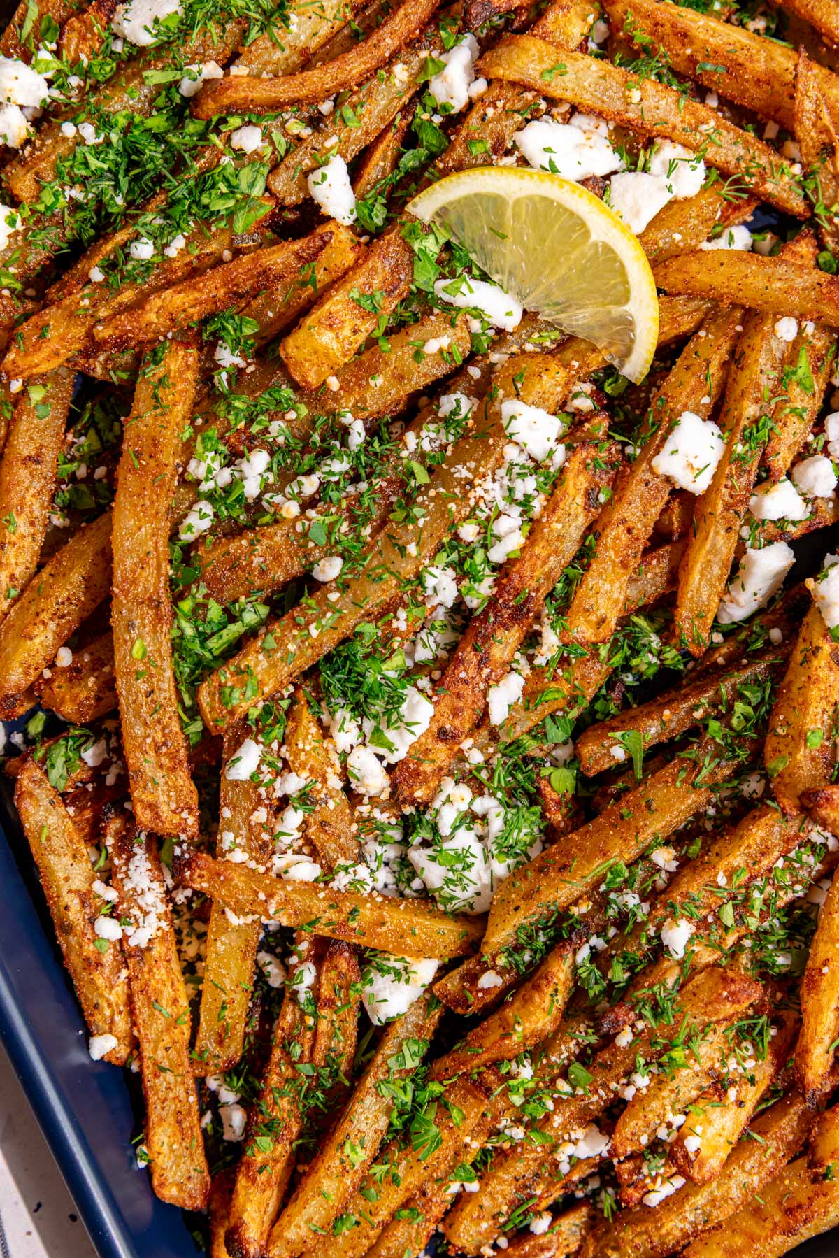 A close up view of the texture of the herbs and feta on a tray of loaded greek feta fries.
