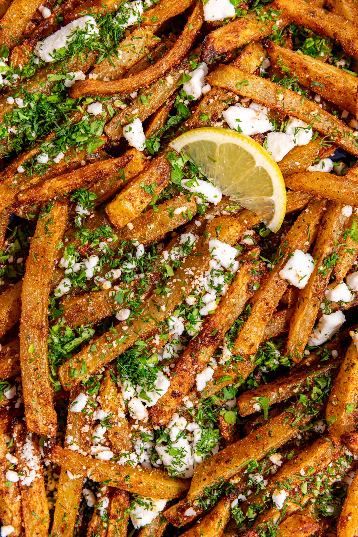 A close up view of the texture of the herbs and feta on a tray of loaded greek feta fries.
