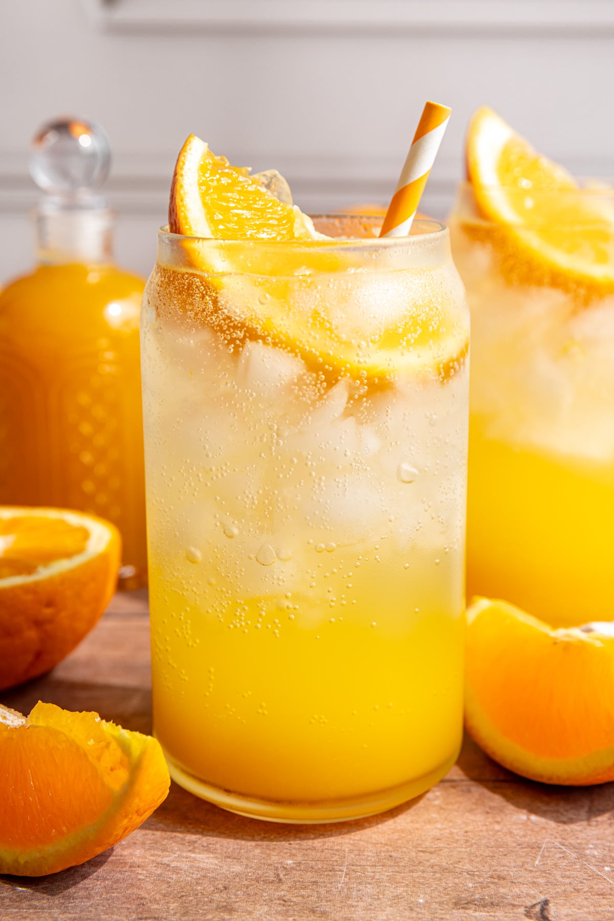 A soda glass of orange cream soda, garnished with an orange wedge and orange striped straw.