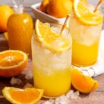 A soda glass of orange cream soda, garnished with an orange wedge and orange striped straw.