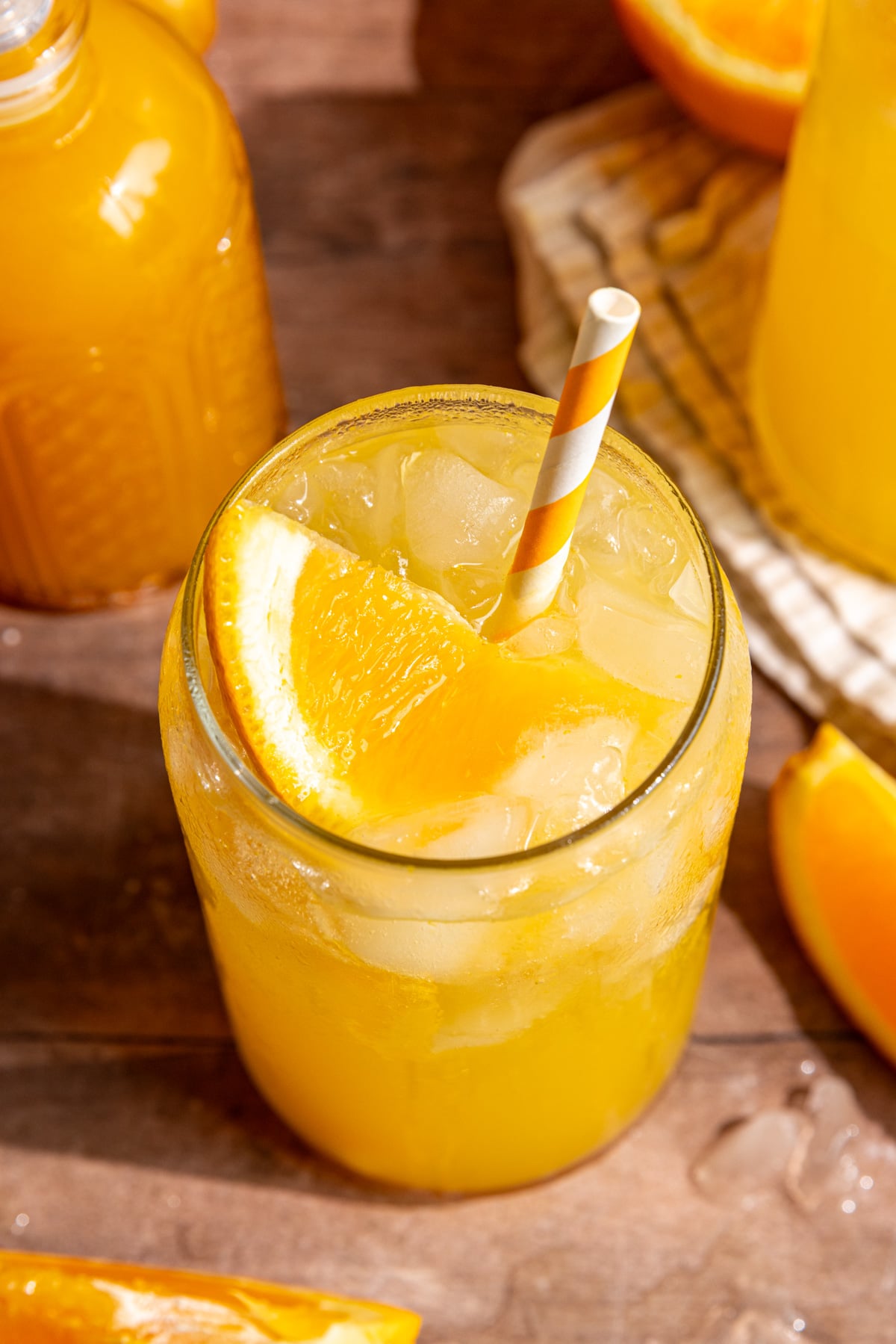 A soda glass of orange cream soda, garnished with an orange wedge and orange striped straw.