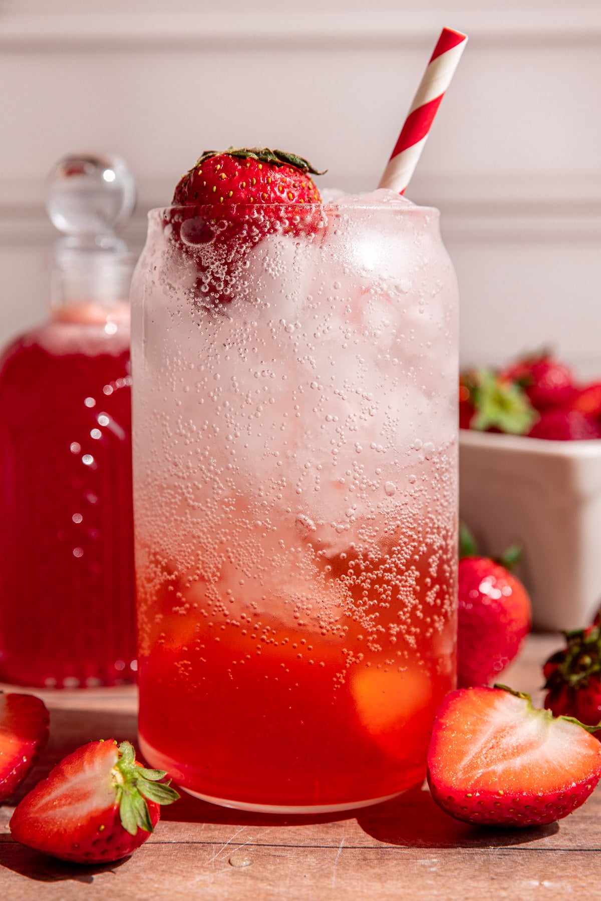 A soda glass of strawberry cream soda garnished with a strawberry and a red striped straw.