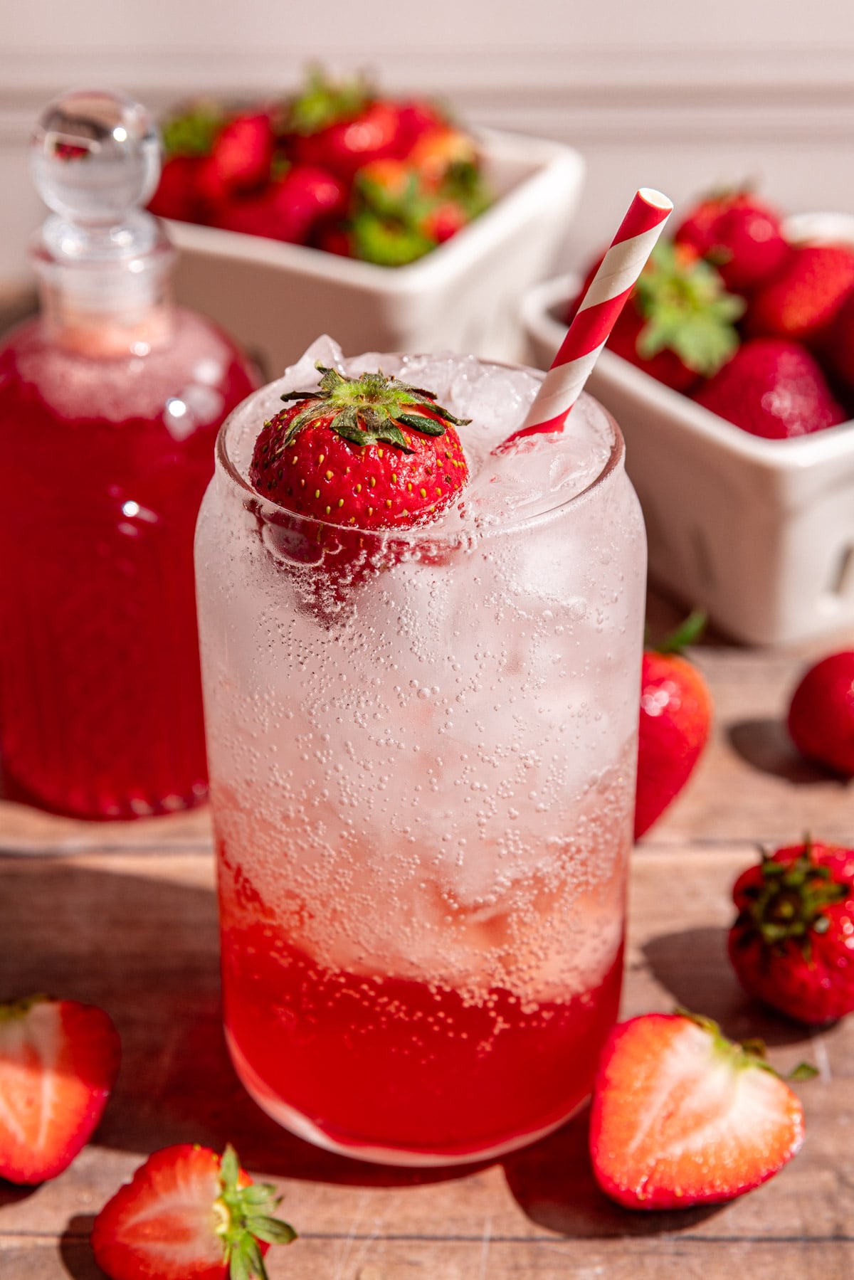 A soda glass of strawberry cream soda garnished with a strawberry and a red striped straw.