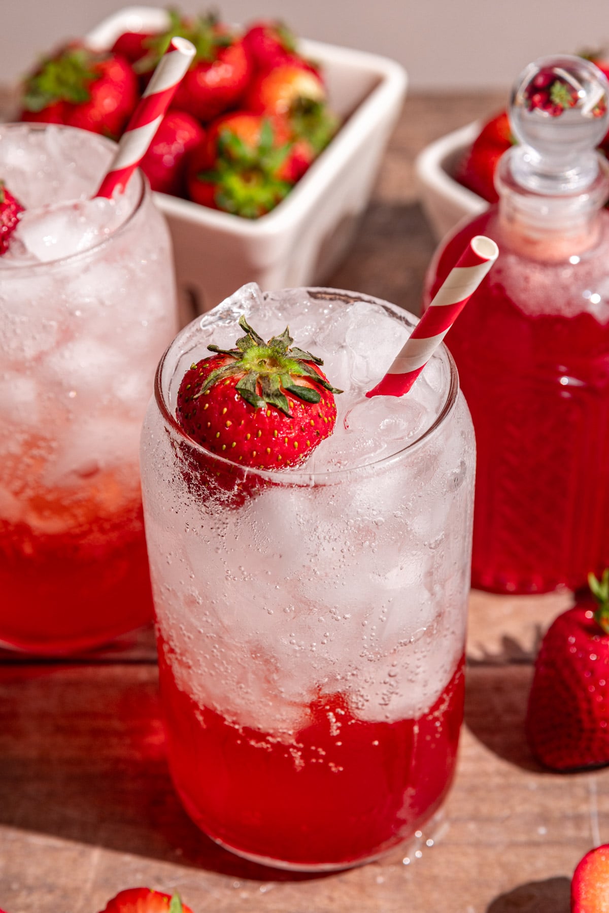 A soda glass of strawberry cream soda garnished with a strawberry and a red striped straw.