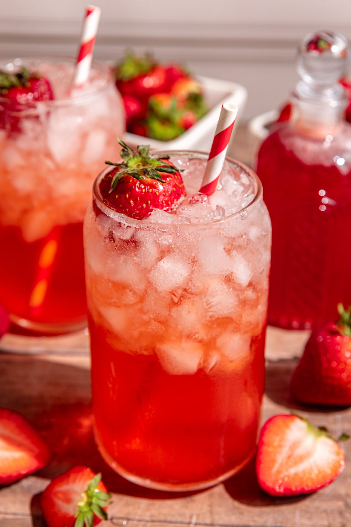 A soda glass of strawberry cream soda garnished with a strawberry and a red striped straw.