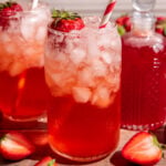 A soda glass of strawberry cream soda garnished with a strawberry and a red striped straw.