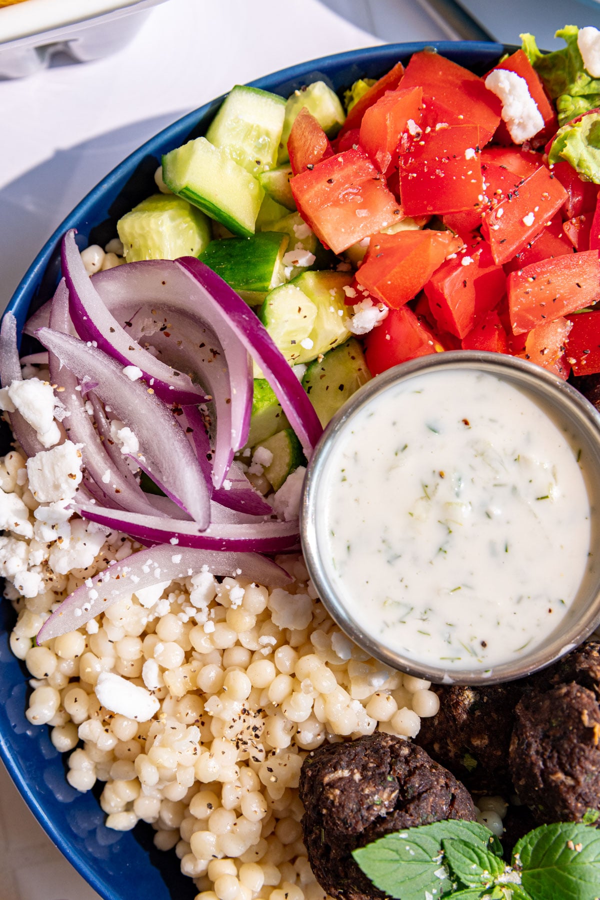 A close up view of the onion, cucumbers, and tomatoes in a vegan Greek couscous bowl.