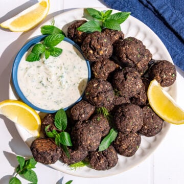 A plate of vegan Greek meatballs, garnished with fresh mint, served with tzatziki.