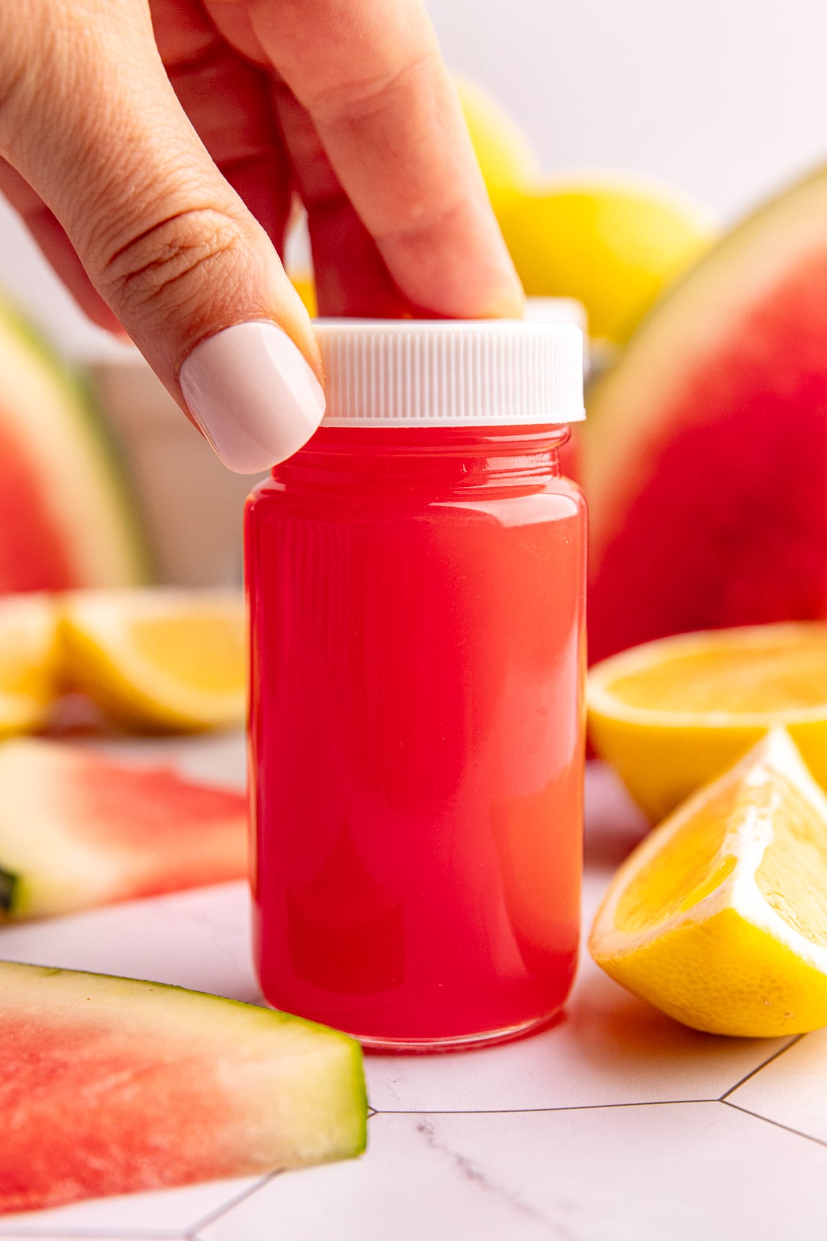 A watermelon ginger wellness shot on a countertop with fresh lemons and watermelon slices.
