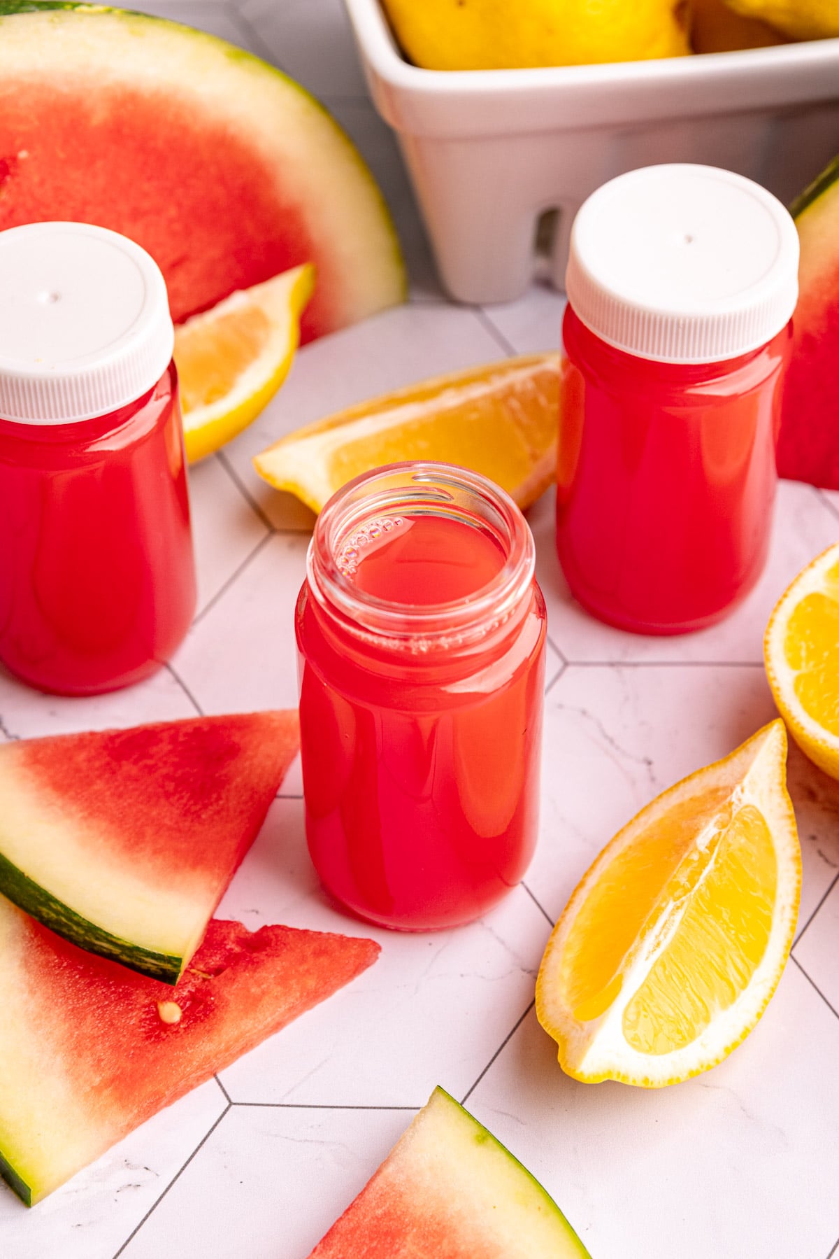 Watermelon ginger wellness shots on a countertop with fresh lemons and watermelon slices.