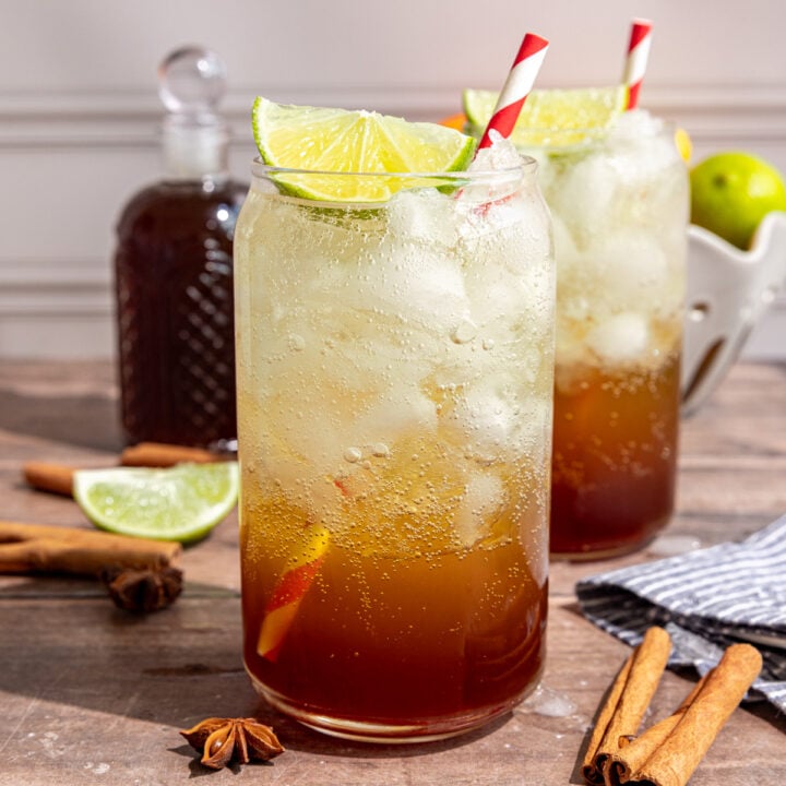 A glass of homemade cola garnished with a lime wedge and red striped straw