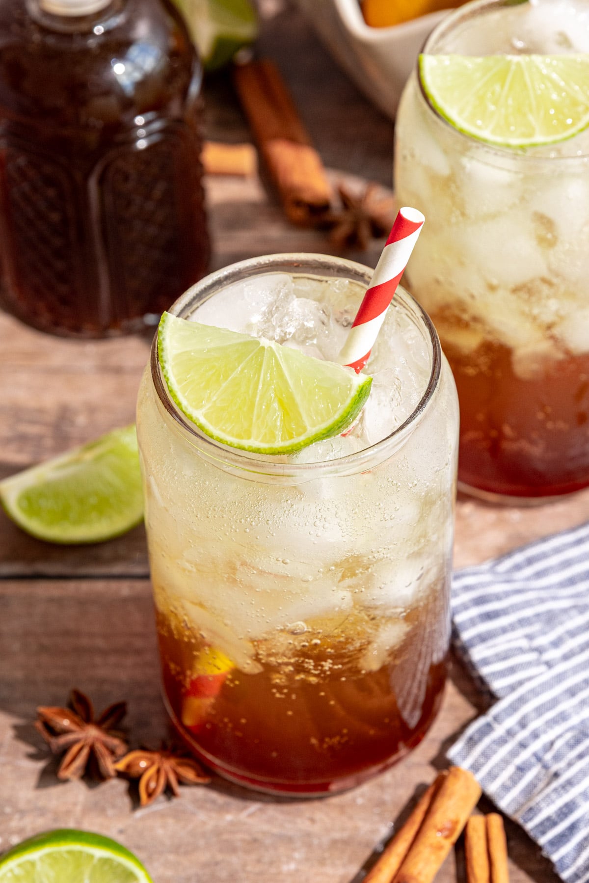 A glass of homemade cola garnished with a lime wedge and red striped straw
