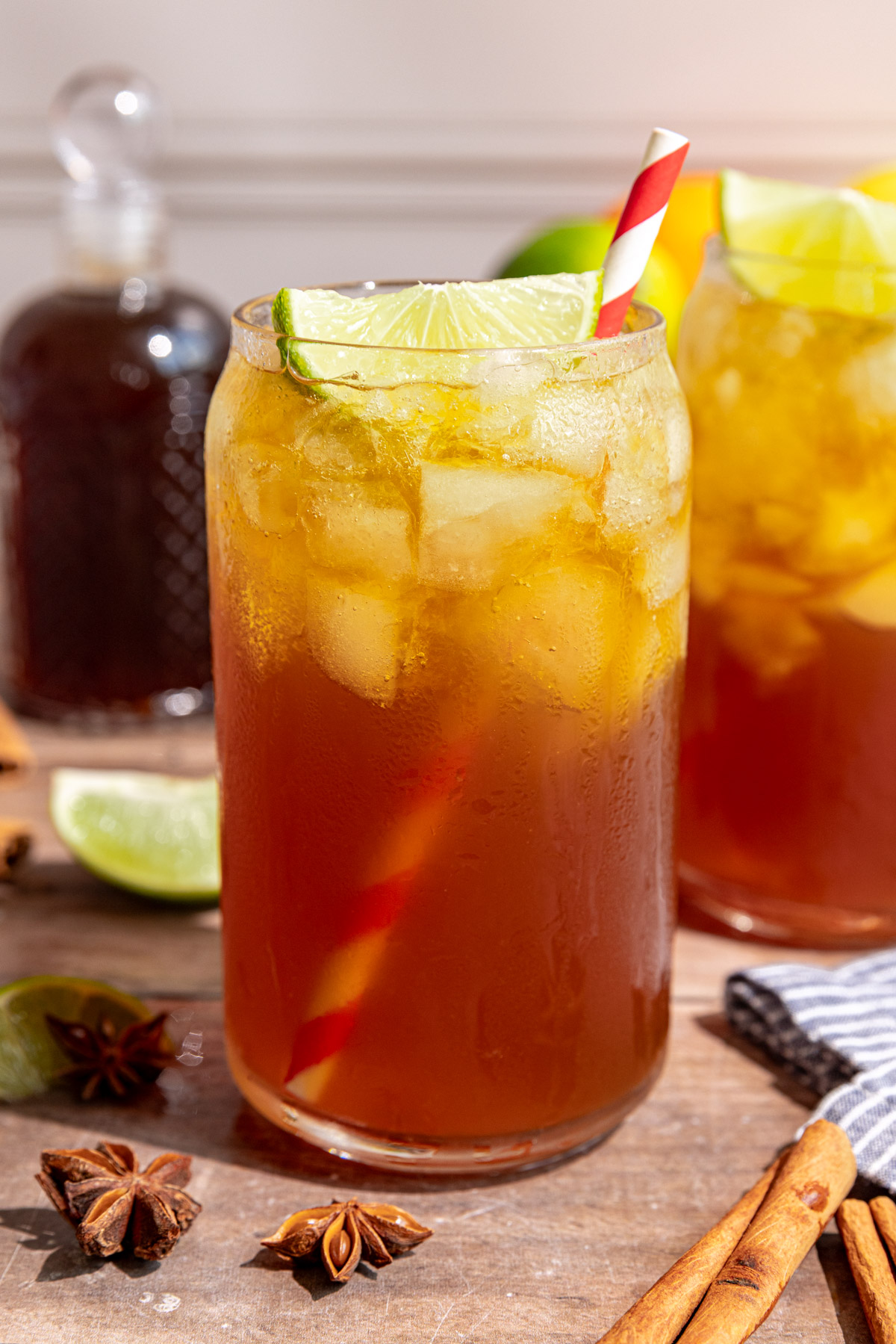 A glass of homemade cola garnished with a lime wedge and red striped straw
