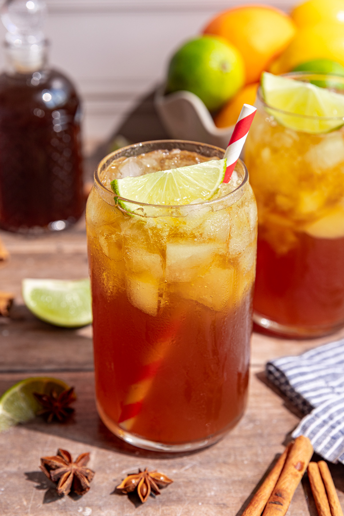 A glass of homemade cola garnished with a lime wedge and red striped straw
