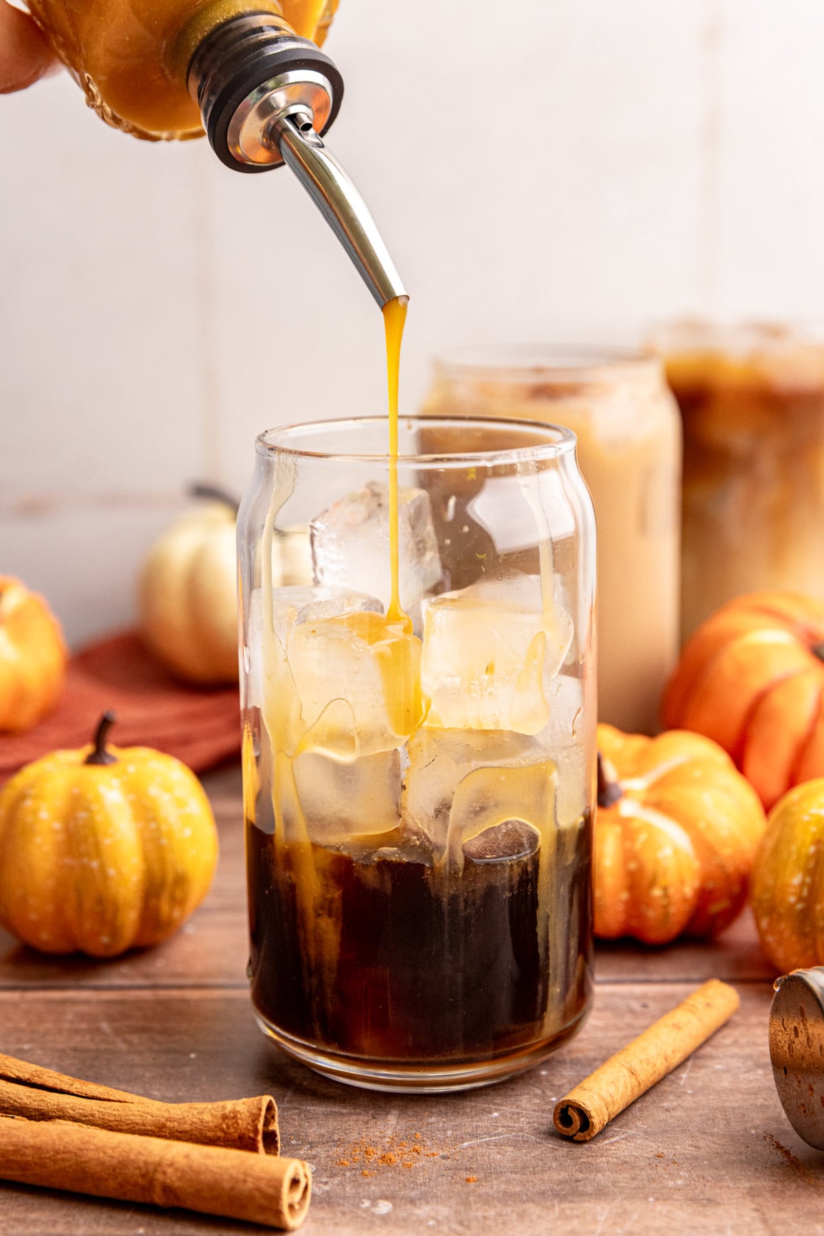 Syrup being poured into a glass while making an iced Starbucks-Style Pumpkin Spice Latte.