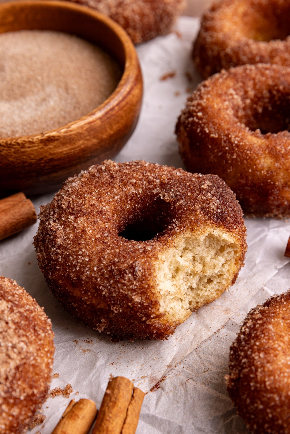A vegan cinnamon sugar cake donut on a piece of parchment paper, with a bite taken out.