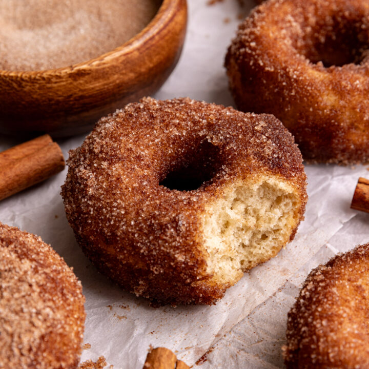 A vegan cinnamon sugar cake donut on a piece of parchment paper, with a bite taken out.