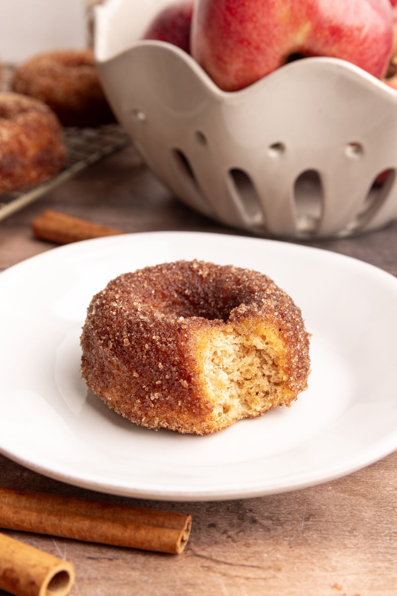An apple cider cake donut on a plate, with a bite taken out.