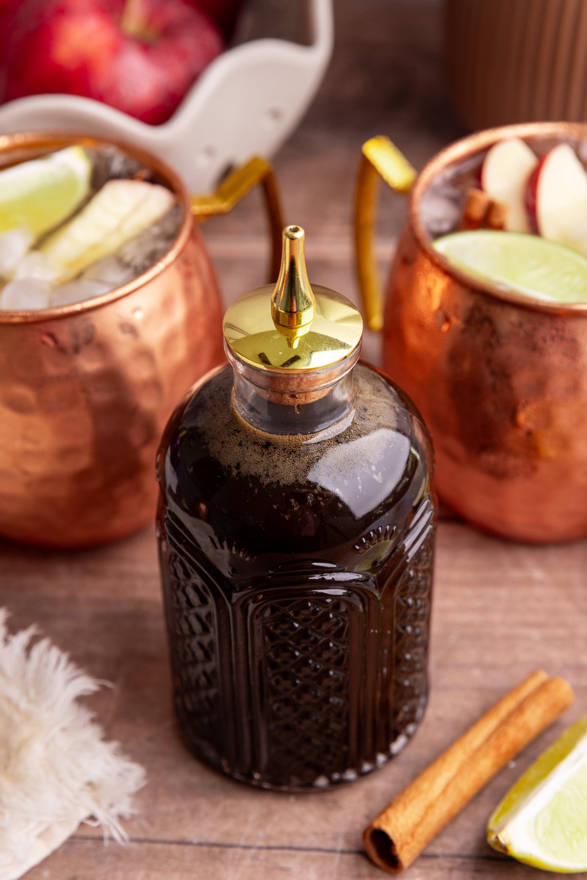 A bottle of coconut sugar syrup next to two glasses of Caramel Apple Mule Mocktail