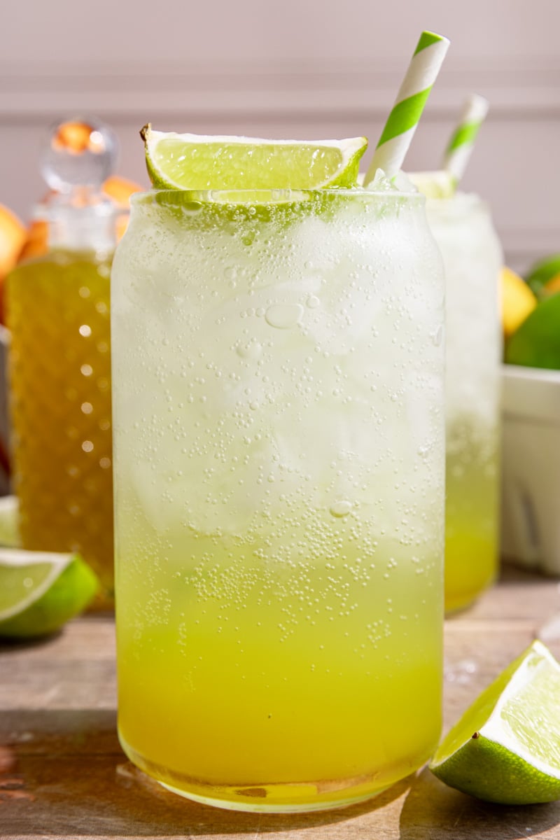 A soda glass of homemade mountain dew, garnished with a lime wedge and green striped straw.