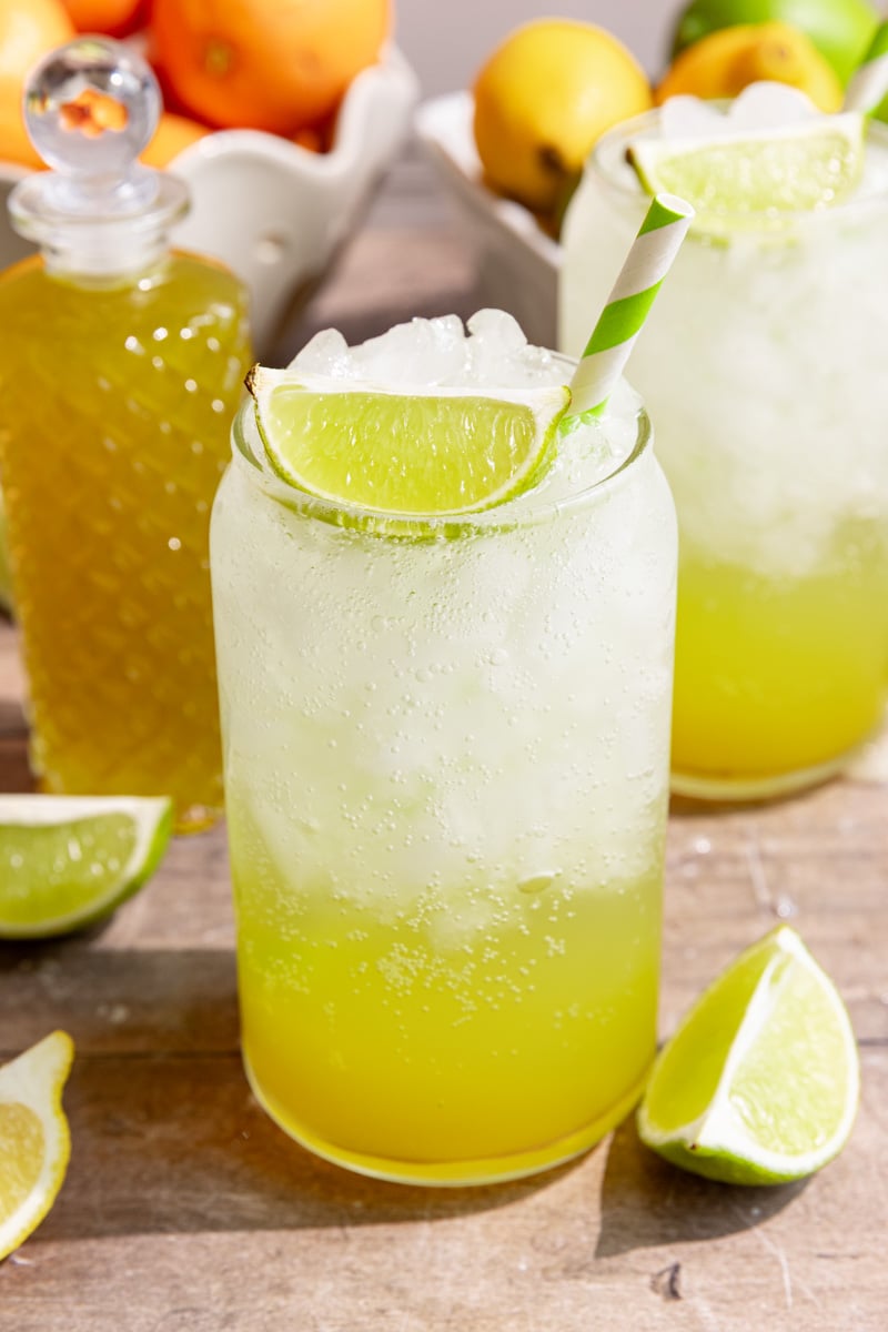 A soda glass of homemade mountain dew, garnished with a lime wedge and green striped straw.