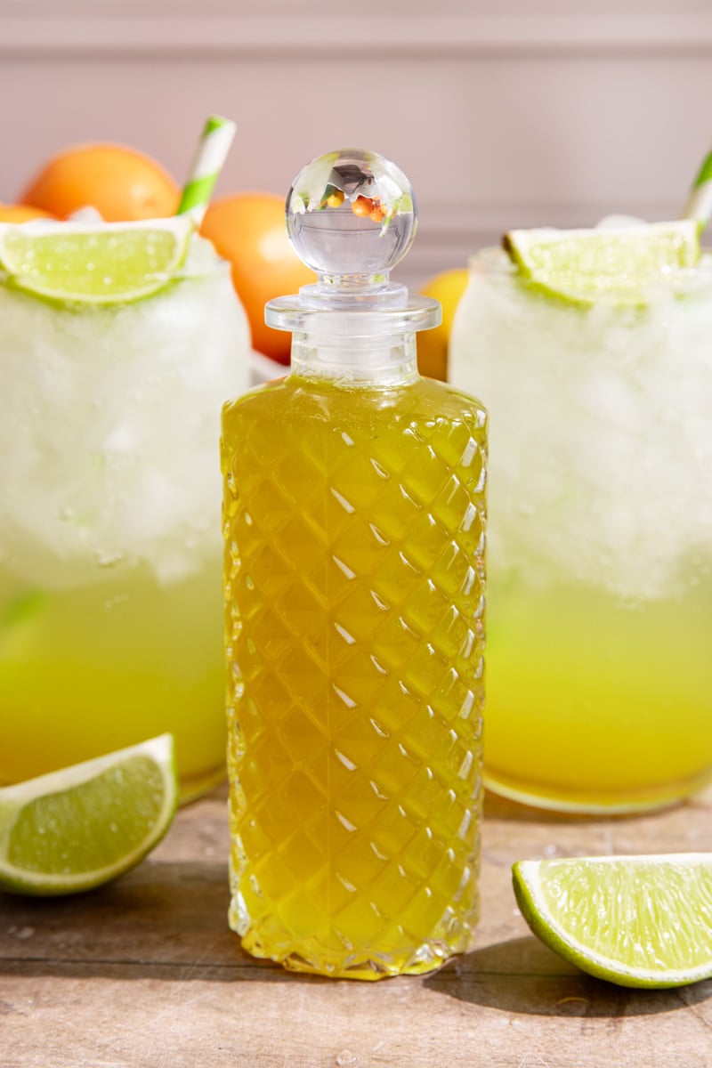 A bottle of homemade mountain dew syrup next to two glasses of mountain dew.