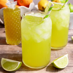 A soda glass of homemade mountain dew, garnished with a lime wedge and green striped straw.