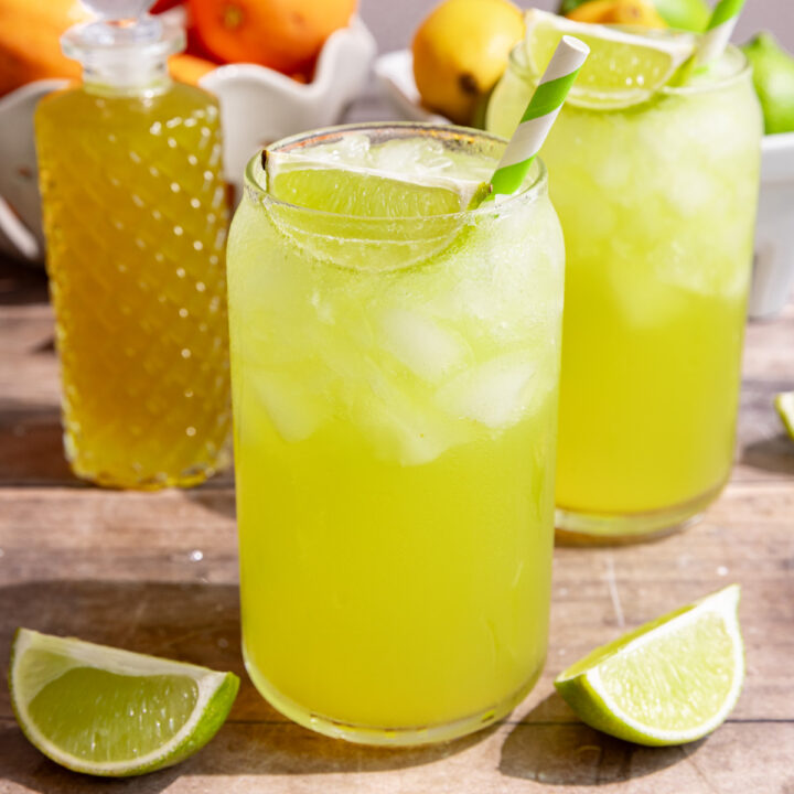 A soda glass of homemade mountain dew, garnished with a lime wedge and green striped straw.