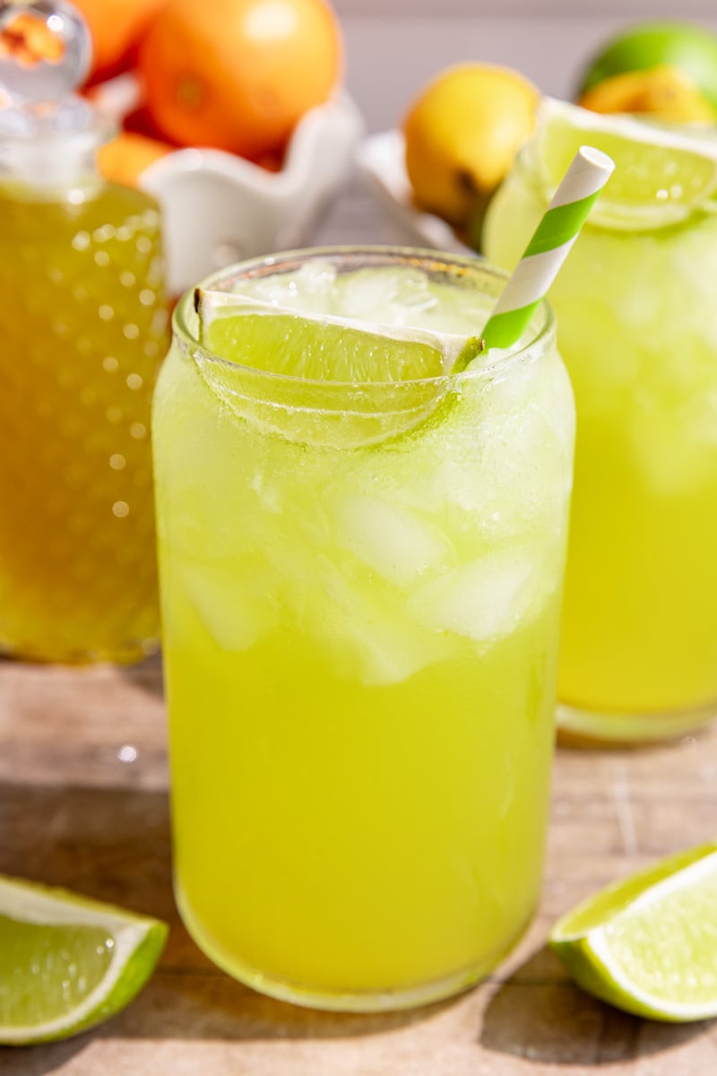 A soda glass of homemade mountain dew, garnished with a lime wedge and green striped straw.