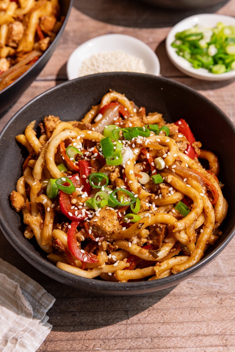 A bowl of vegan sesame noodles, garnished with scallions and sesame seeds.