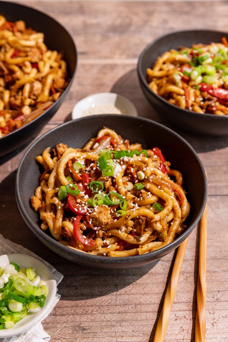 Several bowls of vegan sesame noodles, garnished with scallions and sesame seeds.