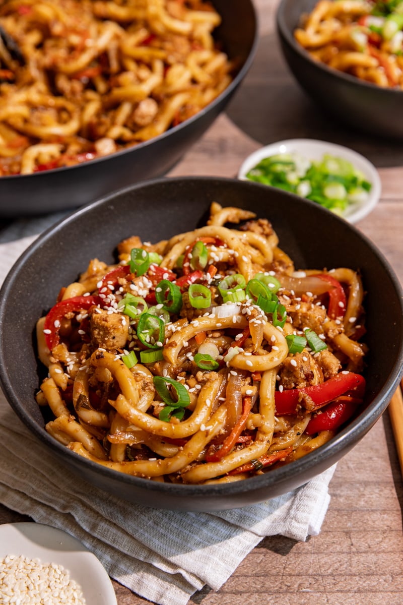 A bowl of vegan sesame noodles, garnished with scallions and sesame seeds.