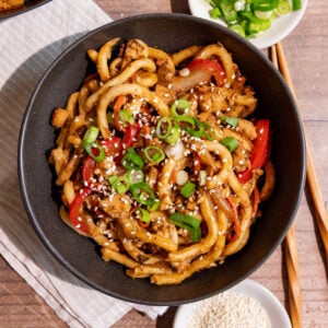 A bowl of vegan sesame noodles, garnished with scallions and sesame seeds.