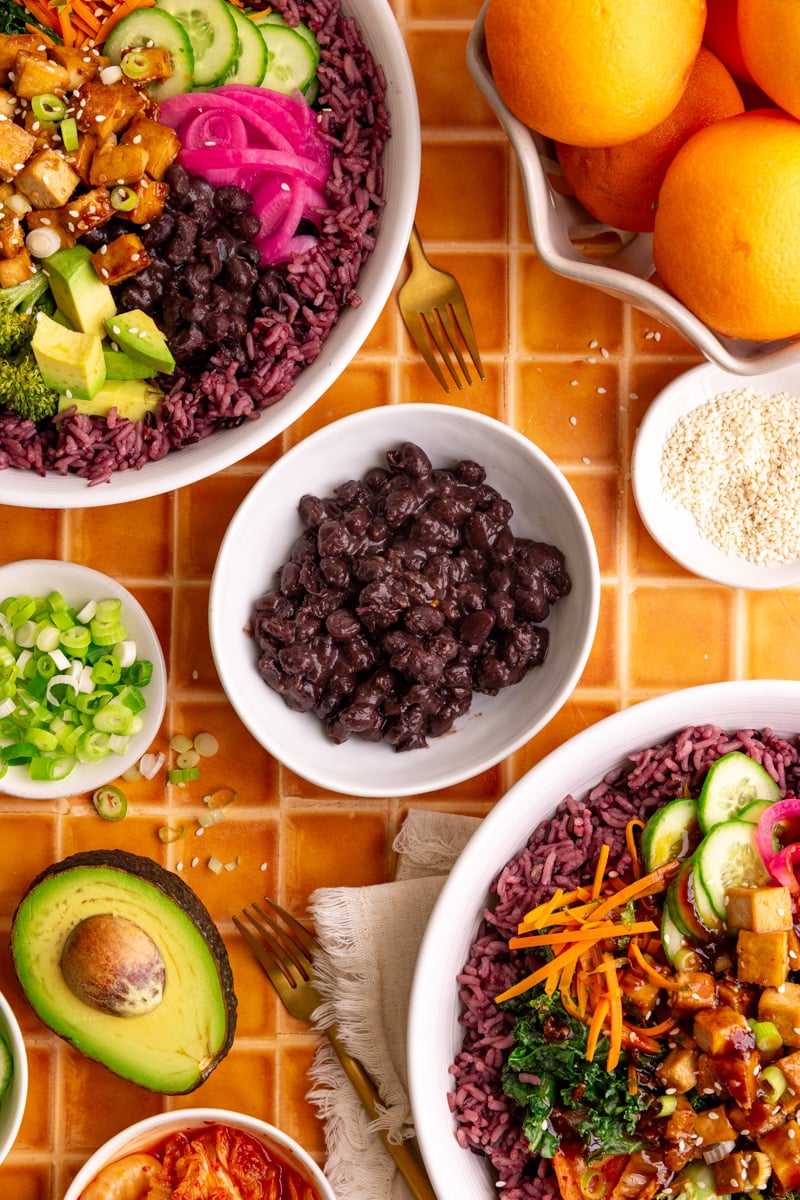 A bowl of homemade black beans, next to two bibibop-style bowls.