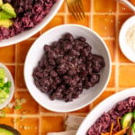 A bowl of homemade black beans, next to two bibibop-style bowls.