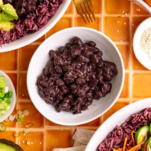 A bowl of homemade black beans, next to two bibibop-style bowls.