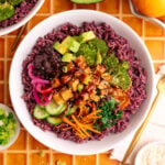 A bibibop style rice bowl with purple rice, sesame broccoli, honey citrus kale, tofu, and other toppings.