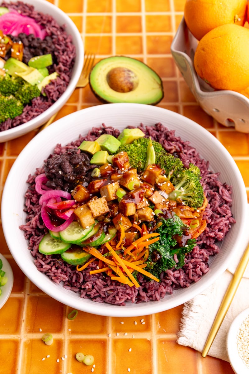 A bibibop style rice bowl with purple rice, sesame broccoli, honey citrus kale, tofu, and other toppings.