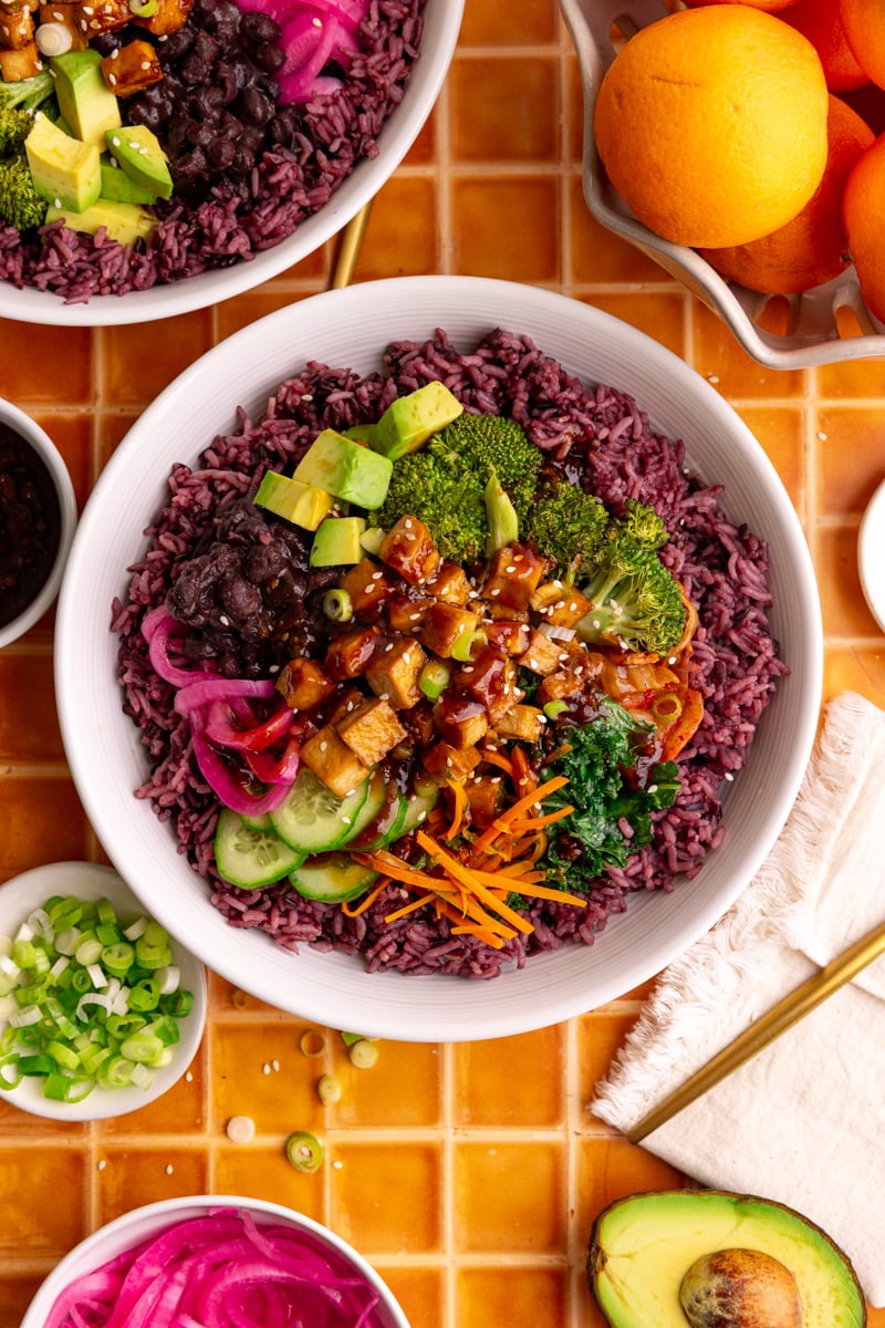 A bibibop style rice bowl with purple rice, sesame broccoli, honey citrus kale, tofu, and other toppings.