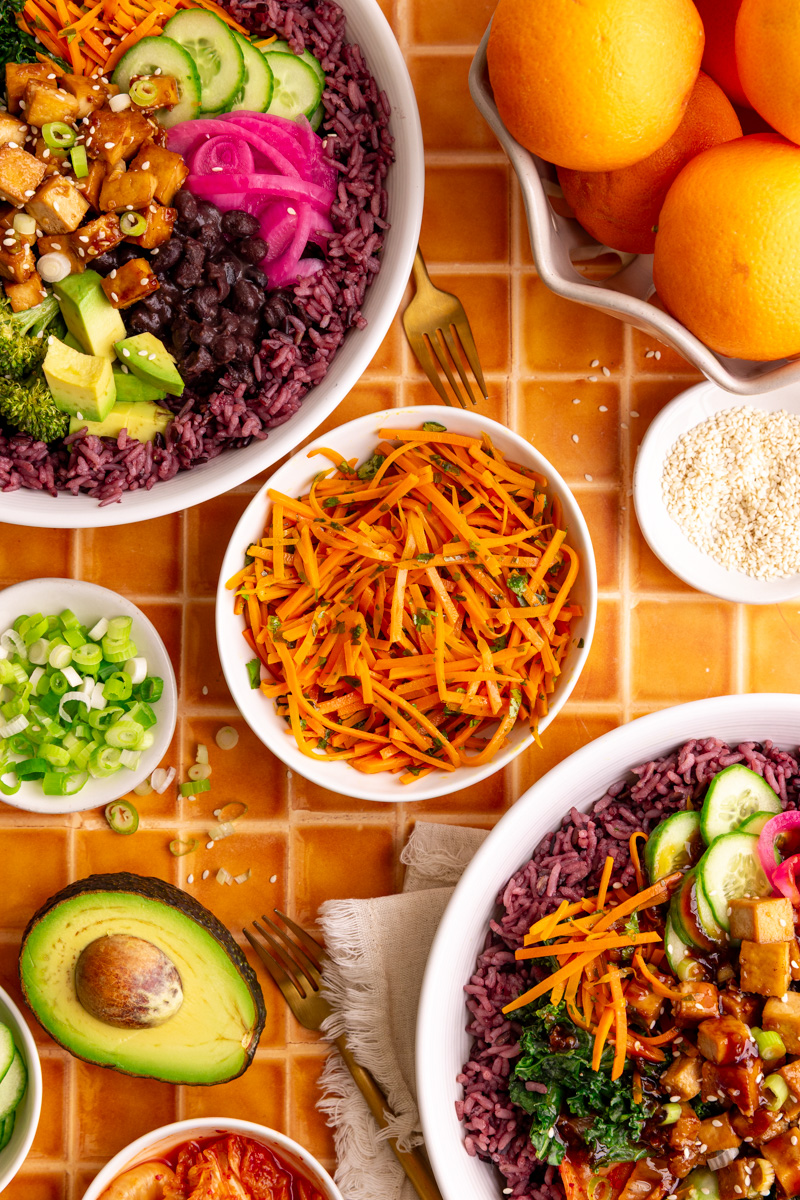 A bowl of bibibop style sesame carrots, with two bibibop-style bowls.