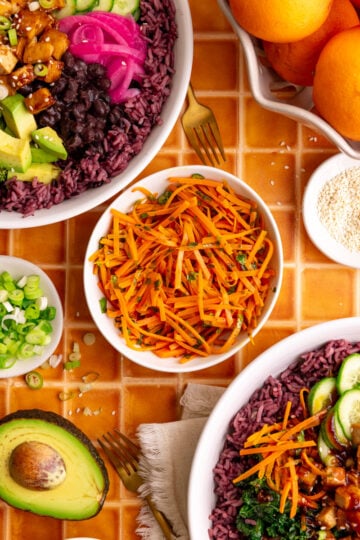 A bowl of bibibop style sesame carrots, with two bibibop-style bowls.