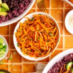 A bowl of bibibop style sesame carrots, with two bibibop-style bowls.