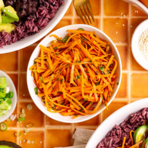 A bowl of bibibop style sesame carrots, with two bibibop-style bowls.
