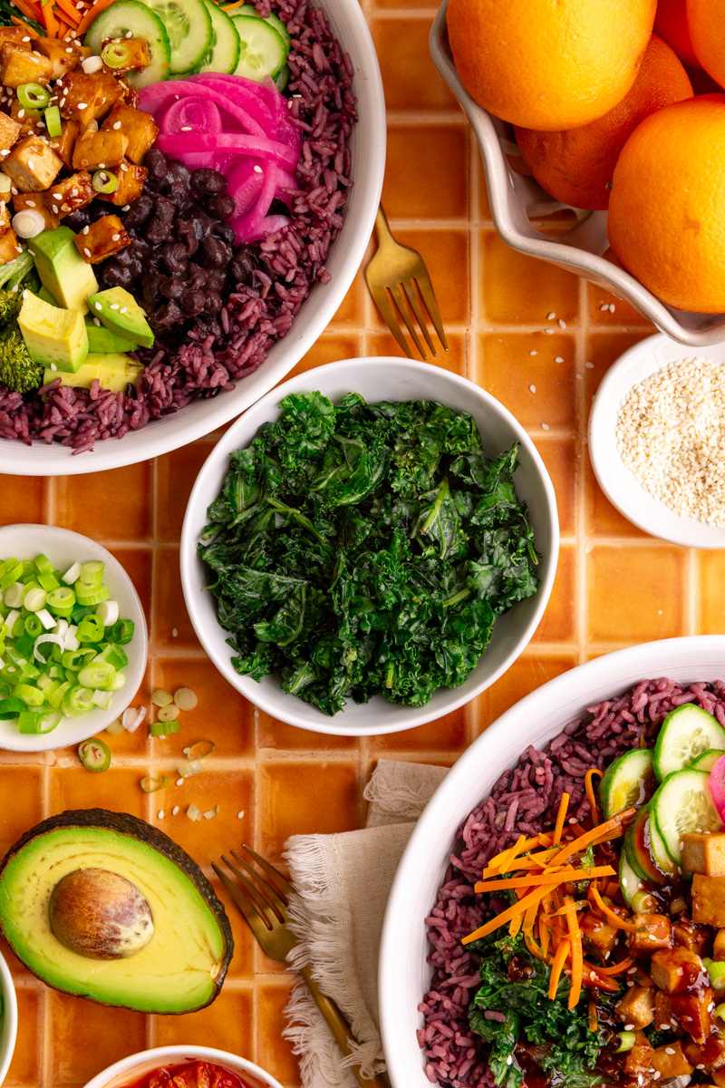 A bowl of bibibop style honey citrus kale, with two bibibop-style bowls.