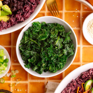 A bowl of bibibop style honey citrus kale, with two bibibop-style bowls.